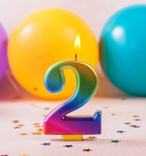 Festive and colorful party setting featuring a glowing number 2 birthday candle, surrounded by vibrant mix of balloons and star-shaped confetti, ideal for anniversary or second birthday celebrations.